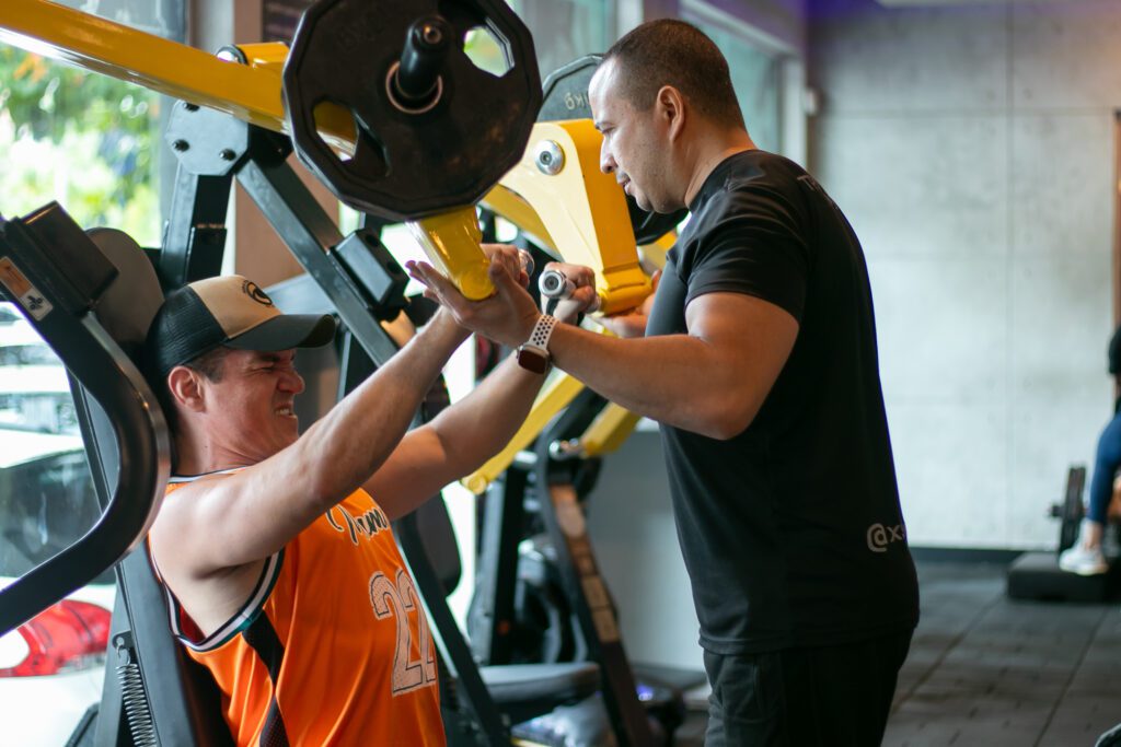 Homem malhando peito na academia auxiliado por personal